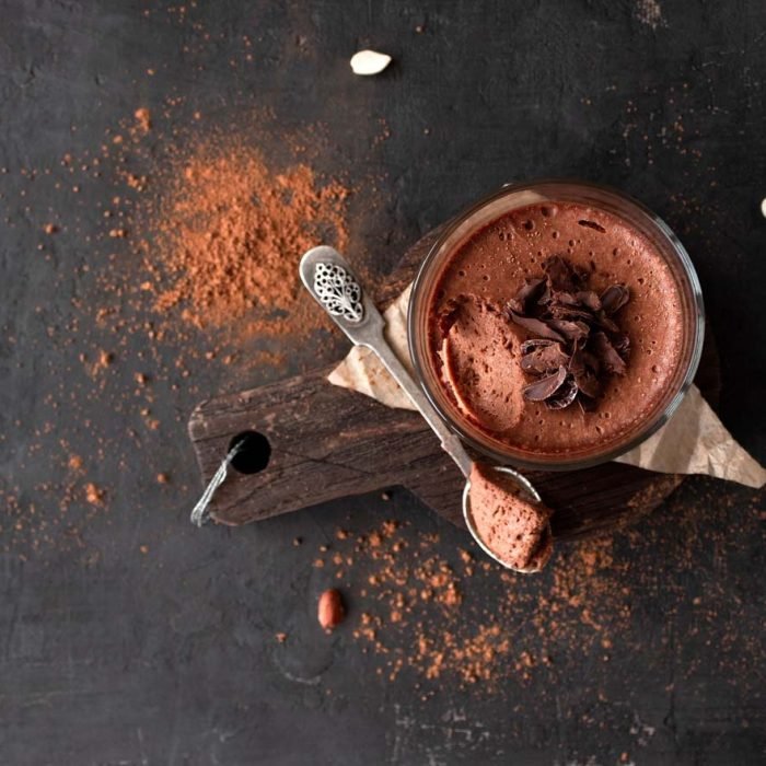 Vegan chocolate mousse glass on a wooden board with a spoon on a dark background. Top view. Flat lay
