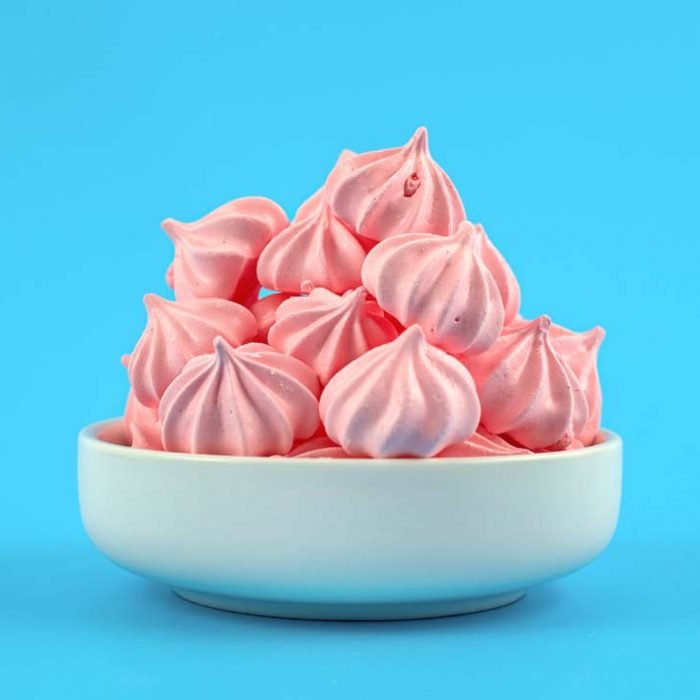 Crispy pink twisted meringues in bowl isolated on blue background